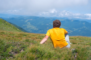 Traveler sitting on an alpine meadow, among lush grass