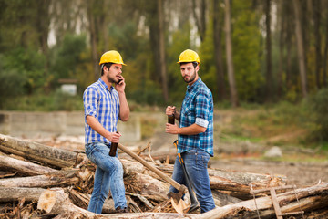 Two guys, with yellow helmets on their heads, rest in the forest after work and drink beer