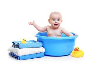 Cute baby in plastic basin, pile of towels and rubber ducks on white background
