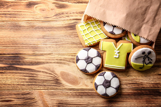 Paper bag with creative cookies decorated in football style on wooden background