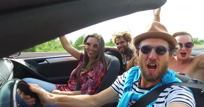 Bearded hipster man with hat driving and singing with friends in convertible