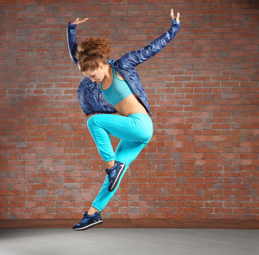 Beautiful young hip-hop dancer jumping against brick wall