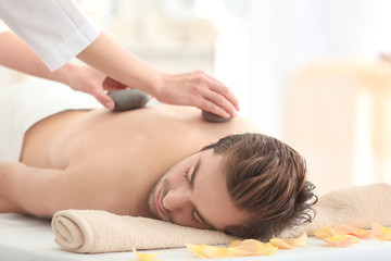 Obraz na płótnie Canvas Young man having stones massage in spa salon