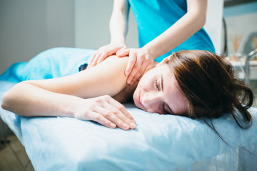 Obraz na płótnie Canvas Close up young woman lying vestured turquoise towel while massage therapist massaging her shoulders. Beauty, health life and cosmetology concept.