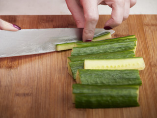 Woman cutting cucumbers for sushi.