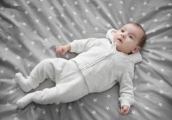 Cute baby in warm clothes lying on bed