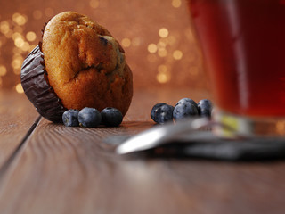 Blueberries and a muffin on a table, cup of tea out of focus in foreground, glittery background.