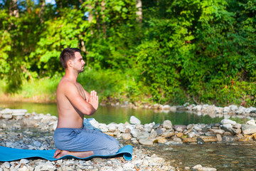 Man meditating near the mountain river. Yoga practicing outdoors.