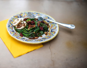Green wilted spinach salad on colorful plate with neutral background