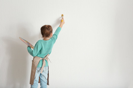 Cute little girl painting on light wall