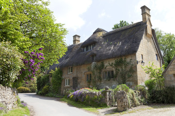 Fototapeta na wymiar Thatched roof, stone cottage with flowering gardens, by a country road, on a summer sunny day .