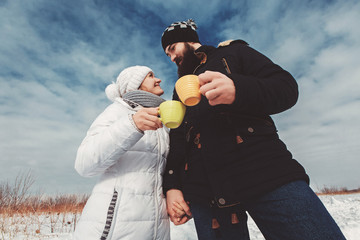 Husband and wife hold hands and drink hot coffee in snowy field