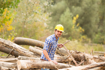 a young man with a yellow helmet on his head cuts wood with saw
