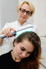 Naklejka premium Doctor examines scalp a pretty young girl with special instrument UV lamp. Skin problems, dermatology, shingles, psoriasis, redness, prevention