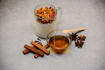 Granola with dried berries, candied fruits, nuts, yogurt, golden honey, anise, cinnamon sticks and cloves on a stone grunge background. Healthy breakfast, dieting and detox concept with copy space