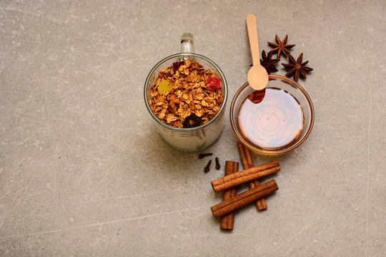 Granola with dried berries, candied fruits, nuts, yogurt, golden honey, anise, cinnamon sticks and cloves on a stone background. Healthy breakfast, dieting and detox concept with copy space
