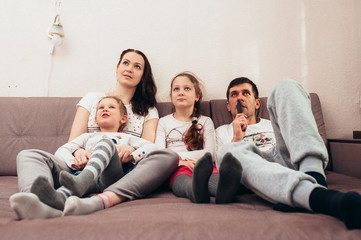 The family is sitting on the couch and watching TV