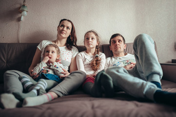 The family is sitting on the couch and watching TV