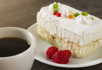 A cup of coffee with cake and raspberries on a dark table.