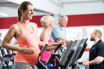 Fototapeta na wymiar Schwangere Frau und Senioren trainieren am Crosstrainer im Fitnessstudio