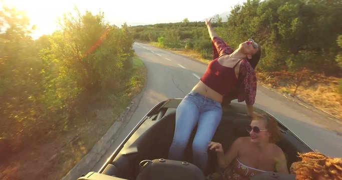 Beautiful brunette sitting on hood of convertible riding with her friends