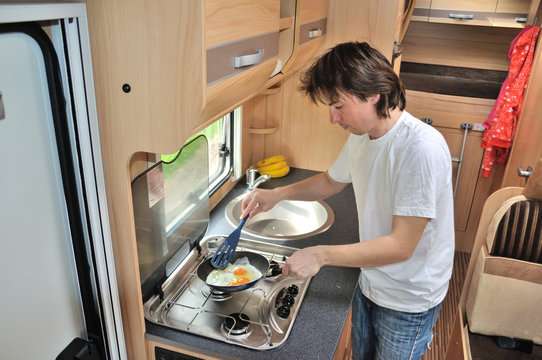 Family vacation, RV holiday trip, travel and camping, man cooking in camper, motorhome interior
