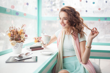 Beautiful happy pretty young woman sitting in a cafe with tablet and mobile phone. Spring trendy pink and blue colors. Flowers and books on the table.