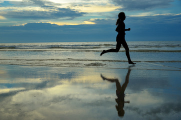 Silhouette of woman jogger running on sunset beach with reflection, fitness and sport concept
