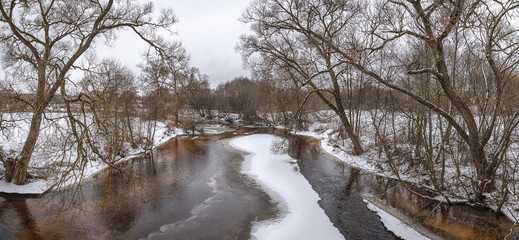 Fototapeta na wymiar Panorama. Spring, the beginning of March. Melts the ice on the river. The shore is covered with snow, trees in the snow. Seasons - spring.