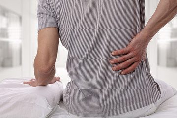 Man suffering from back pain at home in the bedroom. Uncomfortable mattress and pillow causes back...