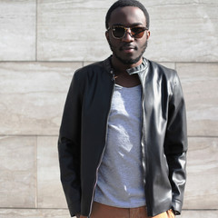 Fashion african man wearing a sunglasses, black rock leather jacket over textured gray background evening in city