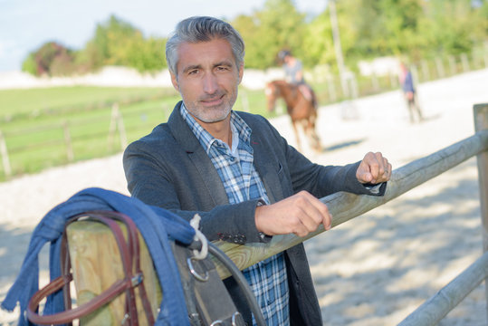 Man leaning on fence in equestrian arena