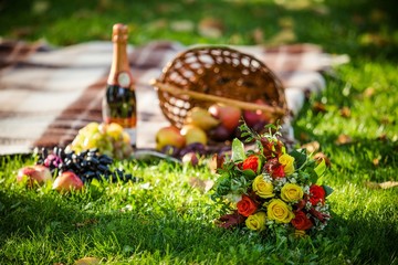 Wker basket with bouquet of flowers, bottle wine on the grass.