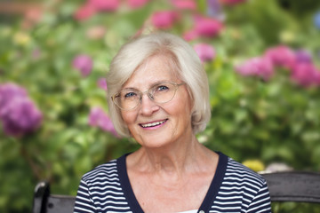 Charmante Seniorin sitzt im Garten vor einem großen Hortensienbusch