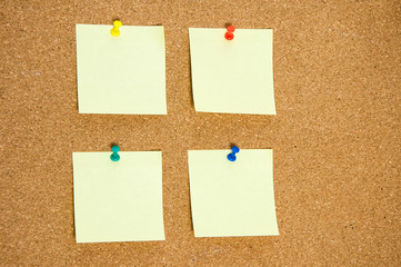 A few blank yellow stickers for taking notes on a cork board close-up.