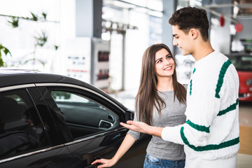Fototapeta na wymiar Beautiful young couple standing at the dealership choosing the car to buy