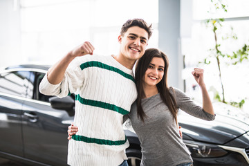 Excited couple buying a car at the dealer with arms up