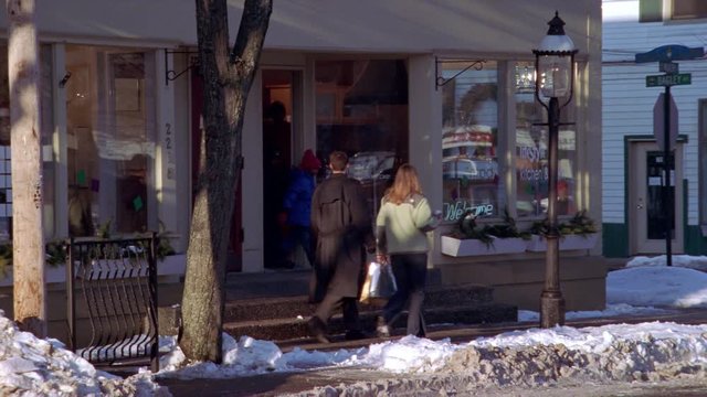 People carrying parcels on a small-town sidewalk edged with snow
