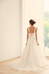 Bride in a beautiful wedding dress standing near window