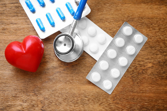 Red heart with stethoscope and pills on table