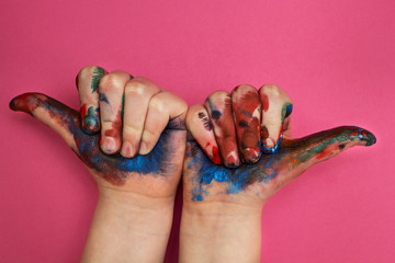 Children's hand, smeared with multicolored paint on a pink background. Finger upward in the rugged sides.