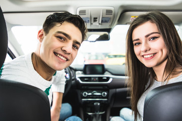 Attractive couple chooses a new car in the showroom, sitting in the car. Back view from car.