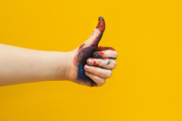 Children's hand, smeared with multicolored paint on a yellow background. Thumbs up. - Powered by Adobe