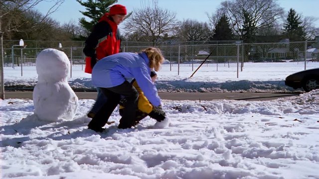 Woman and teenage girl helping child build a snowman