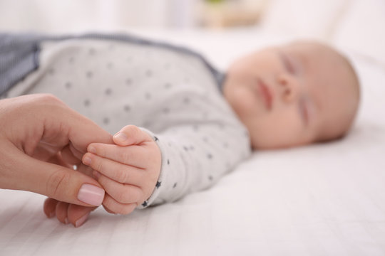 Young woman holding hand of cute sleeping baby, closeup