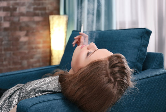 Smoking young woman lying on armchair in living room
