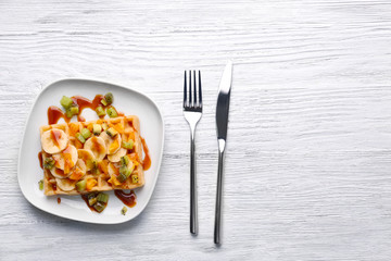 Delicious waffle with fruits and syrup on white plate