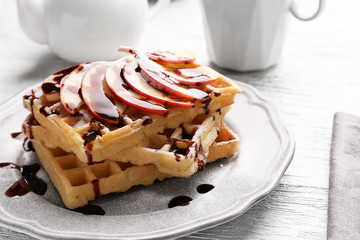 Delicious waffles with apple slices, syrup and sugar powder on plate