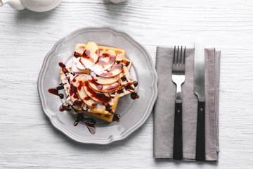 Delicious waffles with apple slices, syrup and sugar powder on plate
