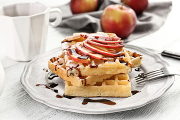 Delicious waffles with apple slices, syrup and sugar powder on plate